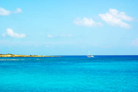 Seascape with coast of Cyprus and cliffs and yacht in distance against blue skyの写真素材