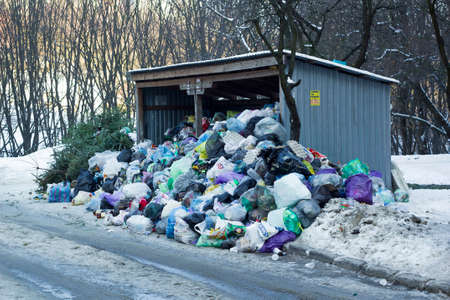 Metal hangar and garbage cans covered of large heap garbage on city streetのeditorial素材