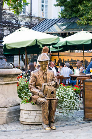 Lviv, Ukraine - July 22, 2017: Living statue gold photographer with camera sits on flower bed with flowers, summer day on cityのeditorial素材