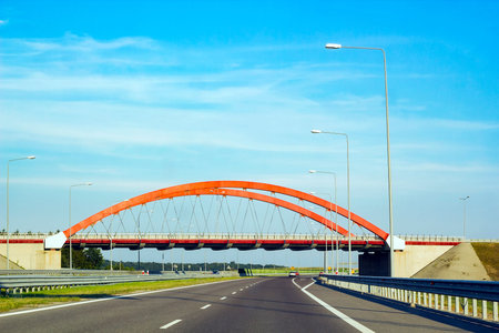 Cars driving on asphalt road. Summer landscape with road, red arch of bridge over track and metal...