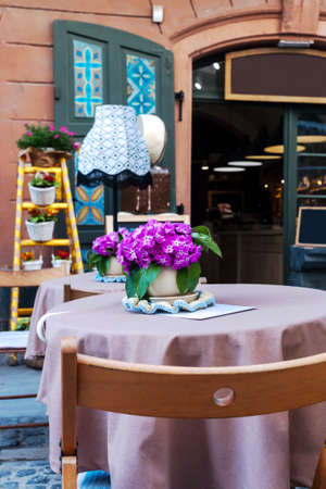 Summer terrace cafe with decorated tables. Table with tablecloth and small vase with decorative bouquet of pink flowersのeditorial素材