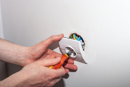 Closeup of electrician hands repairing electric wall socket using screwdriver. Repairman fixing loose electrical outlet boxの写真素材
