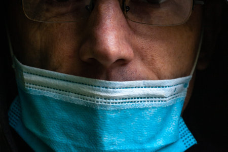 Man in face mask in dark room. Dark portrait of young adult in facemask, selective focus