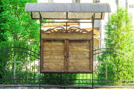 Church wooden empty notice board on city street. Parish council outdoors memo board behind glass. Old wood stand with visor for hanging ads or information in townの写真素材