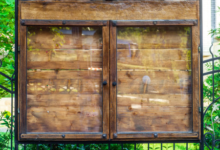 Wooden empty notice board on city street. Outdoor memo board behind glass. Old wood stand with tacks for ads or information closeup. Close up retro signboard for advertisement or news in town parkの写真素材