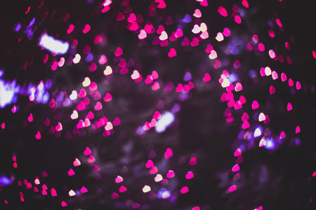 Blurred backgrounds with tiny pink hearts bokeh. Defocused backdrop with romantic neon garland glow...