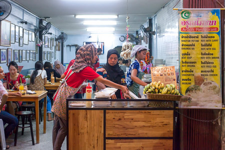 Phuket, Thailand - February 21, 2018: Open street cafeteria with people sitting at tables. Waiters in uniform working and cafe visitors eating. Islam women in hijab work on kitchen, soft focusのeditorial素材