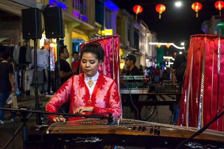 Phuket, Thailand - February 21, 2018: Young woman in red blouse playing string instrument on night city streetのeditorial素材