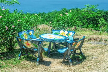 Wooden painted picnic chairs and round table in summer backyard. Dinning woods empty colorful furniture set, green floral bushes and blue sea at sunny light dayの写真素材