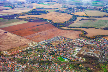 Aerial autumn fields and city of Slovakia, view from flying plane window. Top view shot of slovak countryside, densely populated slovak town with green sports fileld borders large tracts of farmsの写真素材