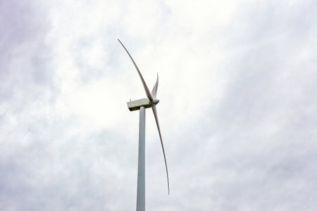 Wind turbine turn by cloudy sky close up, side view. Windmill blade spins against clouds closeup. Power generating tall windturbin rotate against overcast sunset cloudscapeの写真素材