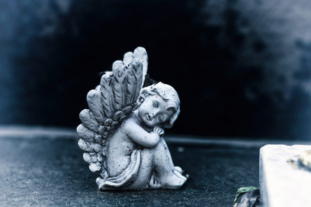 Vintage dirty statue of weep angel on tomb stone in old cemetery. Small ancient winged angelic...