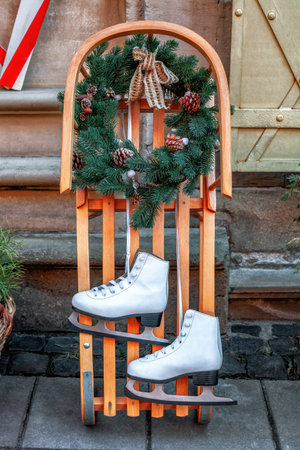 Two figure ice skates, wooden sledge, Christmas wreath . Pair white leather skate shoes hanging,...