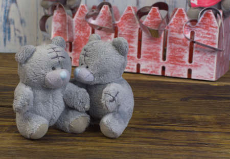 small soft toys of bears on a wooden floor against the background of an out of focus red fence with hearts on itの写真素材