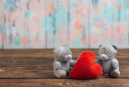 two little toy bears with a heart on a wooden floor on a background out of focus on a light background with hearts in the form of bokehの写真素材