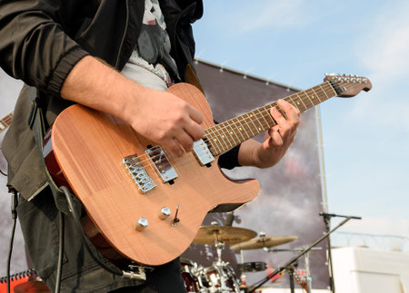musician playing six-string electric guitar guitar at street concert against defocused background