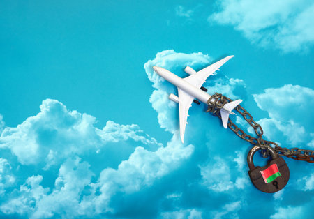 concept - model of a passenger airliner on a metal chain and a lock against a background of clouds