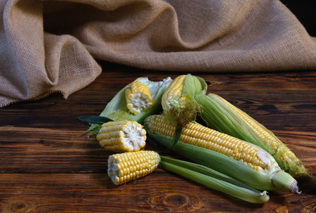 ripe ears of corn with leaves on an old wooden table and burlap in the background