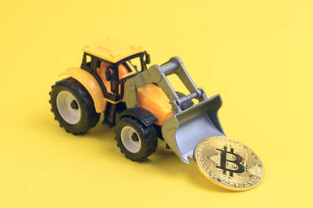 a toy bulldozer on a yellow background, holding a cryptocurrency coin in a bucket, conceptの写真素材