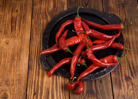 red bitter peppers on a black tray are lying on a wooden tableの写真素材