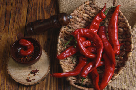 red bitter peppers in a wicker basket on a wooden table, next to a cut of a tree trunk, there is a...