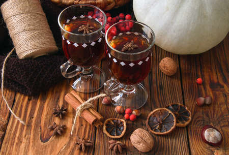 mulled wine in glasses with cardamom stars, cinnamon stick, rowan berries, pumpkin on a wooden table, a spool with twine on a knitted scarfの写真素材