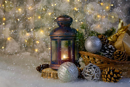 christmas still life, lantern with candles, basket with cones and Christmas tree toys, background bokeh and defocus, snow fallingの写真素材