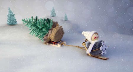 toy girl Snow Maiden, on skis, pulls a forest tree behind her against the background of lei in out-of-focus and bokeh and falling snowの写真素材