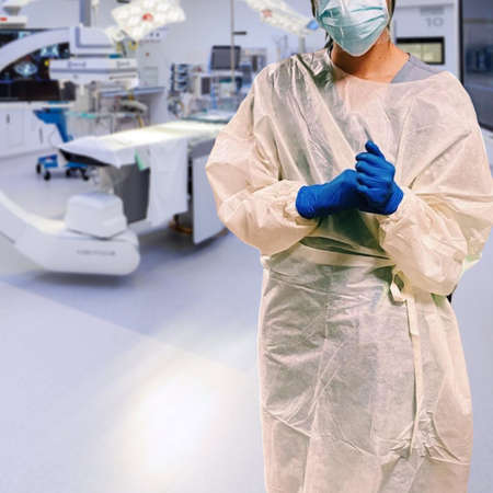 Healthcare worker wearing gloves, mask, face shield, and gown in hospital surgical roomの写真素材