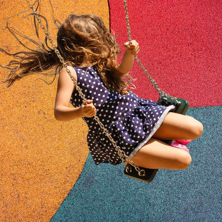 Elementary age girl sitting in a swing flying in the air against a tri-color backgroundの写真素材
