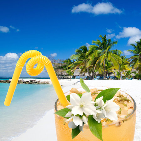 Cold orange Jasmine herbal tea on ice with flower and straw in a glass in the front and beach with...