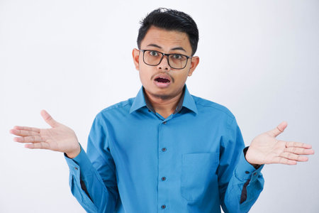 confused handsome young asian man with glasses in wearing shirt shrugging hands sideways and looking disappointed isolated on white backgroundの写真素材