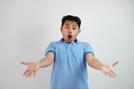 shock asian man with open hands and mouth wearing blue t shirt isolated on white backgroundの写真素材