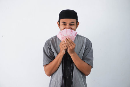 shocked young asian muslim man holding paper money gift (THR) from family ramadan Eid al-Fitr time...