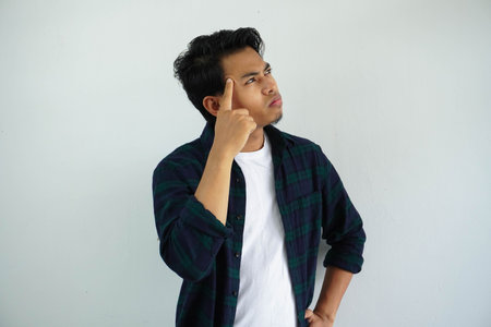 young asian man pointing finger to his head and showing thinking gesture isolated on white...