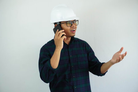 young Asian male engineer wearing white hard hat was talking on a cell phone for construction work...