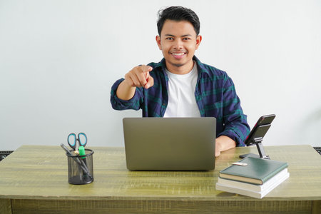 happy a business asian man is sitting at his workplace smiling pointing to the front