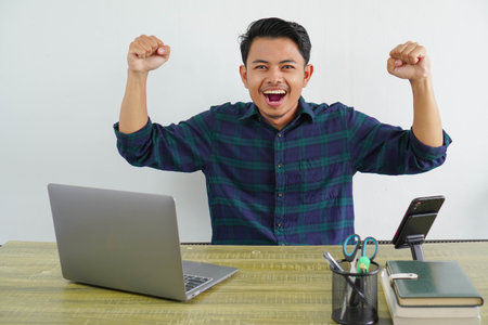 Strong young asian man sit work at wooden desk with pc laptop. Achievement business career lifestyle concept. showing biceps, musclesの写真素材