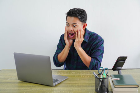 Surprised young asian man sit work at wooden desk with pc laptop. Achievement business career...