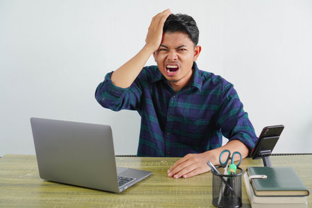 Irritated young asian man sit work at wooden desk with pc laptop. Achievement business career...