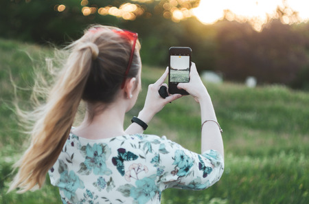 girl is photographing the sunset on the phone back viewの写真素材