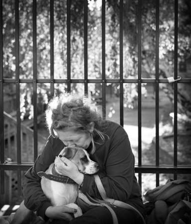 Homeless woman in her fifties with her dog on the sidewalk during an autumn sunset.のeditorial素材