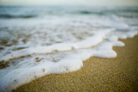 Image of tide rolling onto pristine beach with white sea foam. This image has very narrow depth of field to achieve a dreamy quality.の写真素材