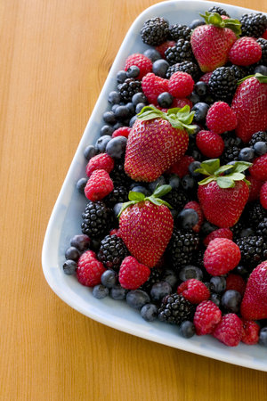 Blueberries, strawberries, raspberries and blackberries on a plate setting on a wooden dining table.の写真素材
