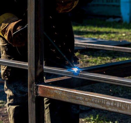 A strong man is a welder, welding mask and welders leathers, a metal product is welded with a arc welding machine at the construction siteの写真素材