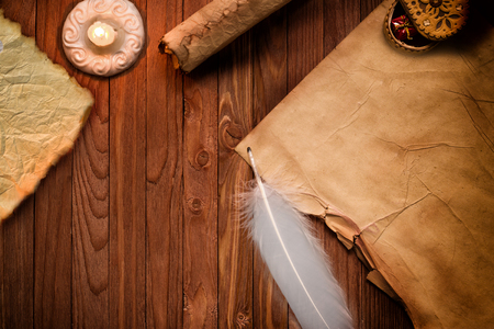 Old blank scroll paper and quill on wooden table illuminated by  candleの写真素材