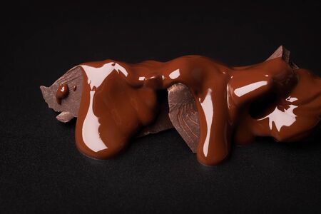 broken pieces pouring with melted chocolate on black tableの写真素材
