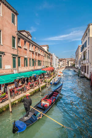 VENICE, ITALY - APRIL 13: Gondolier on gondola in Rio de S.Lorenzo. Open cafe with tourists, Fondamenta S.Lorenzo, Venice, Italy on April 13, 2013のeditorial素材
