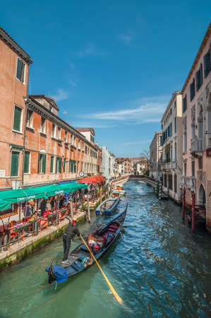 VENICE, ITALY - APRIL 13: Gondolier on gondola in Rio de S.Lorenzo. Open cafe with tourists, Fondamenta S.Lorenzo, Venice, Italy on April 13, 2013のeditorial素材