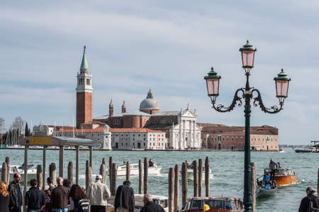 VENICE, ITALY - APRIL 13, 2013 : Tourists waiting gondola on San Marco embankment. Church of San Giorgio Maggiore and ornate lampposts. Venice, Italyのeditorial素材